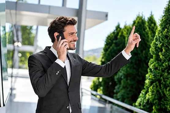 Un homme en costume téléphone et lève un doigt devant un bâtiment moderne.