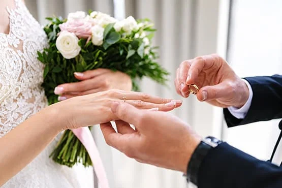 Un homme passe une alliance au doigt d’une mariée tenant un bouquet.