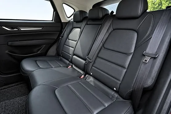 Banquette arrière en cuir noir d’une voiture, avec trois places et leurs ceintures.