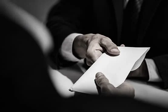 Deux personnes s’échangent une enveloppe blanche, en gros plan et en noir et blanc.